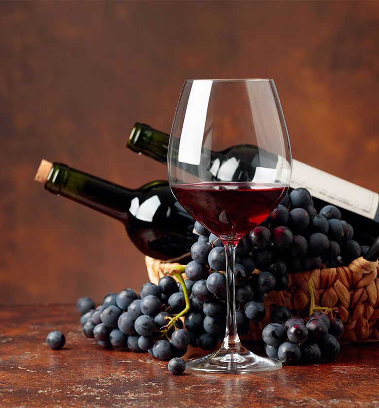 Juicy blue grapes and bottles of red wine on a brown background