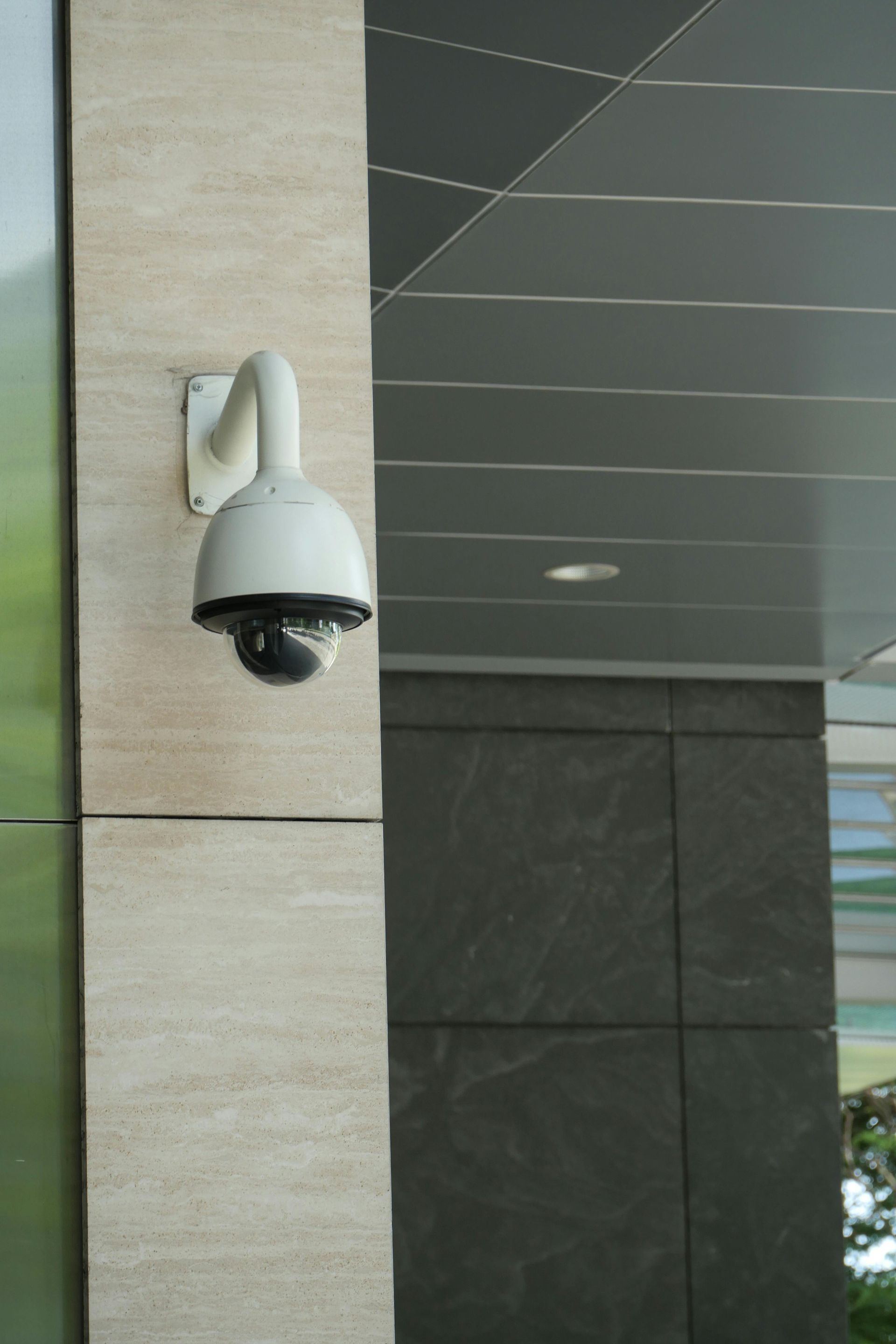 Security camera mounted on a light-colored column, overlooking a building facade. Camera is white with a black dome.