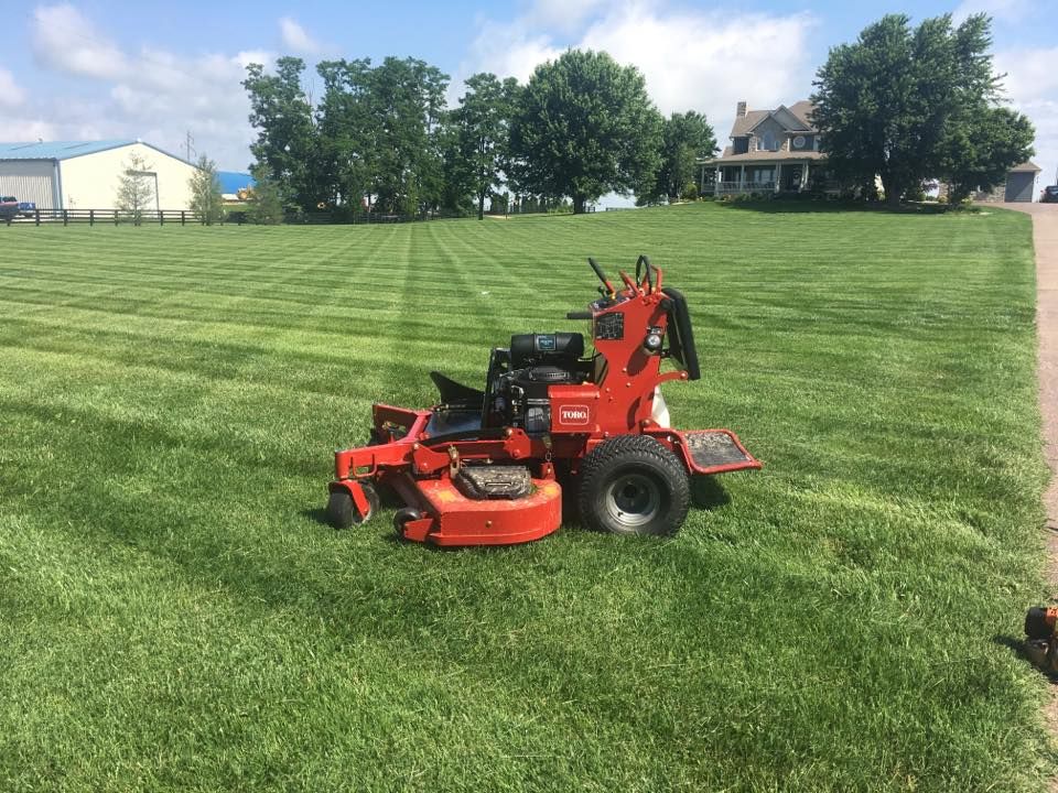 A red lawn mower is sitting in the middle of a lush green field.