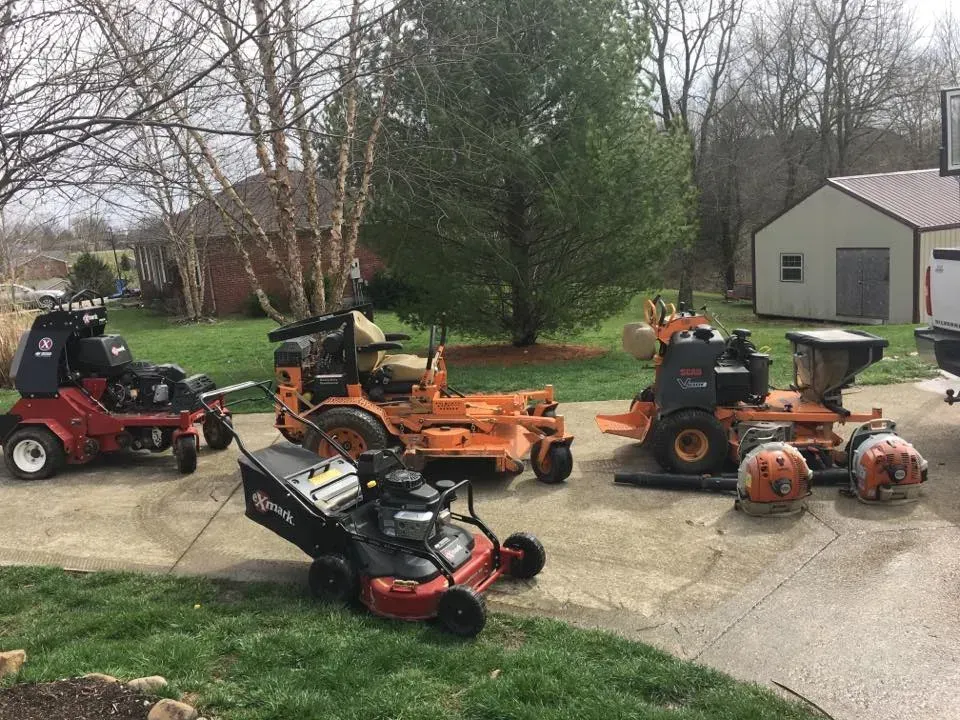 A group of lawn mowers are parked in a driveway.