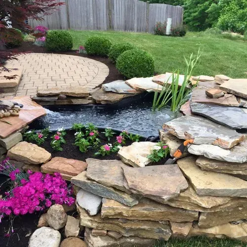 There is a pond in the middle of the garden surrounded by rocks and flowers.