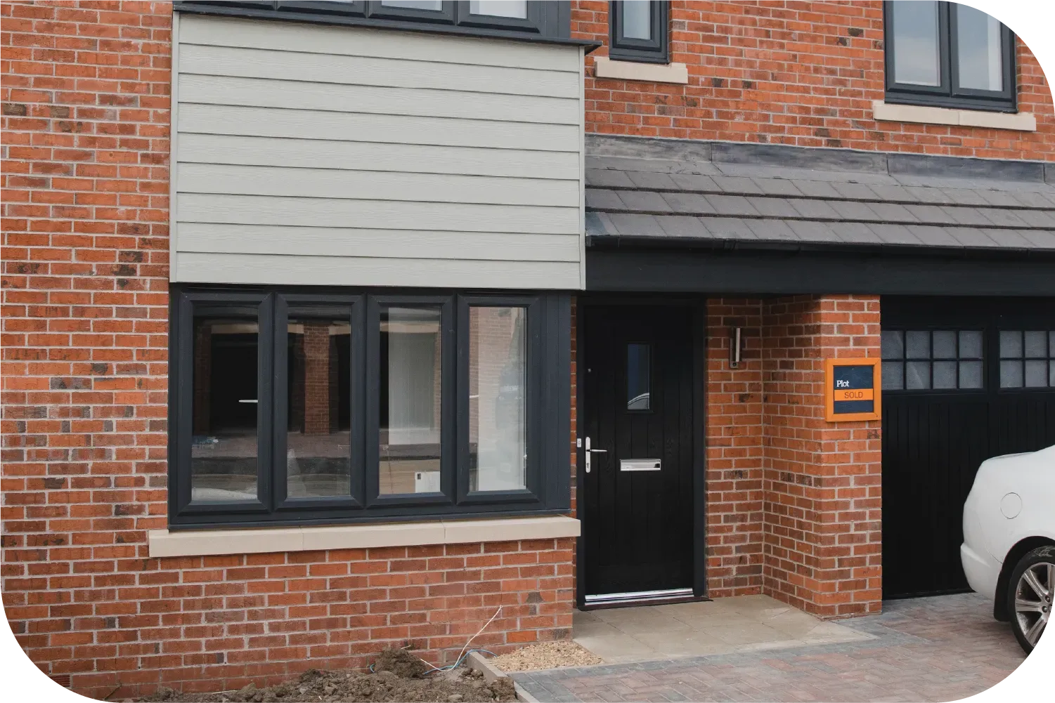 A modern brick house facade featuring a black front door, a multi-pane window, horizontal grey siding, and a garage.