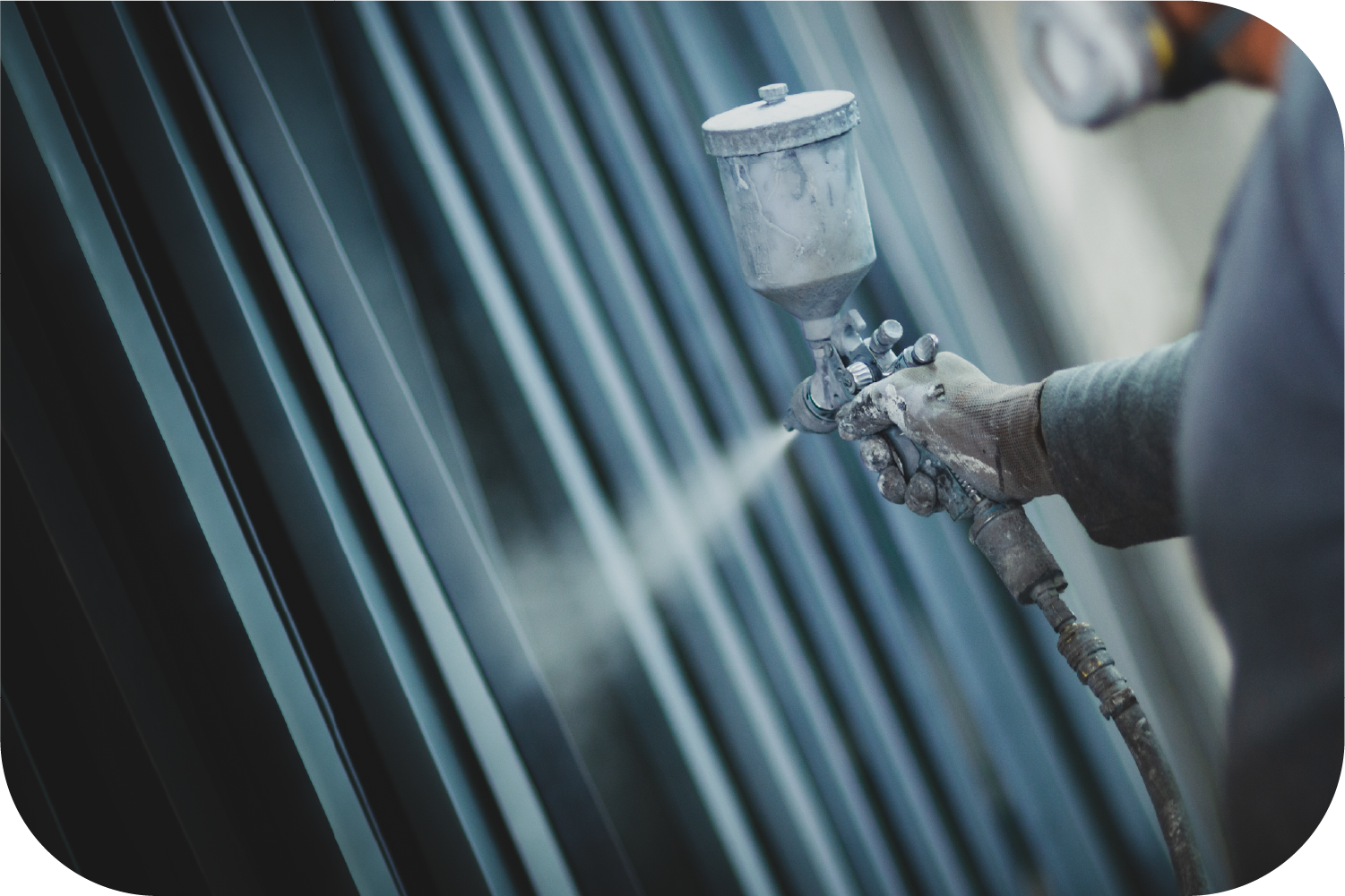 A person uses a spray gun to apply a coating to dark vertical metal panels.