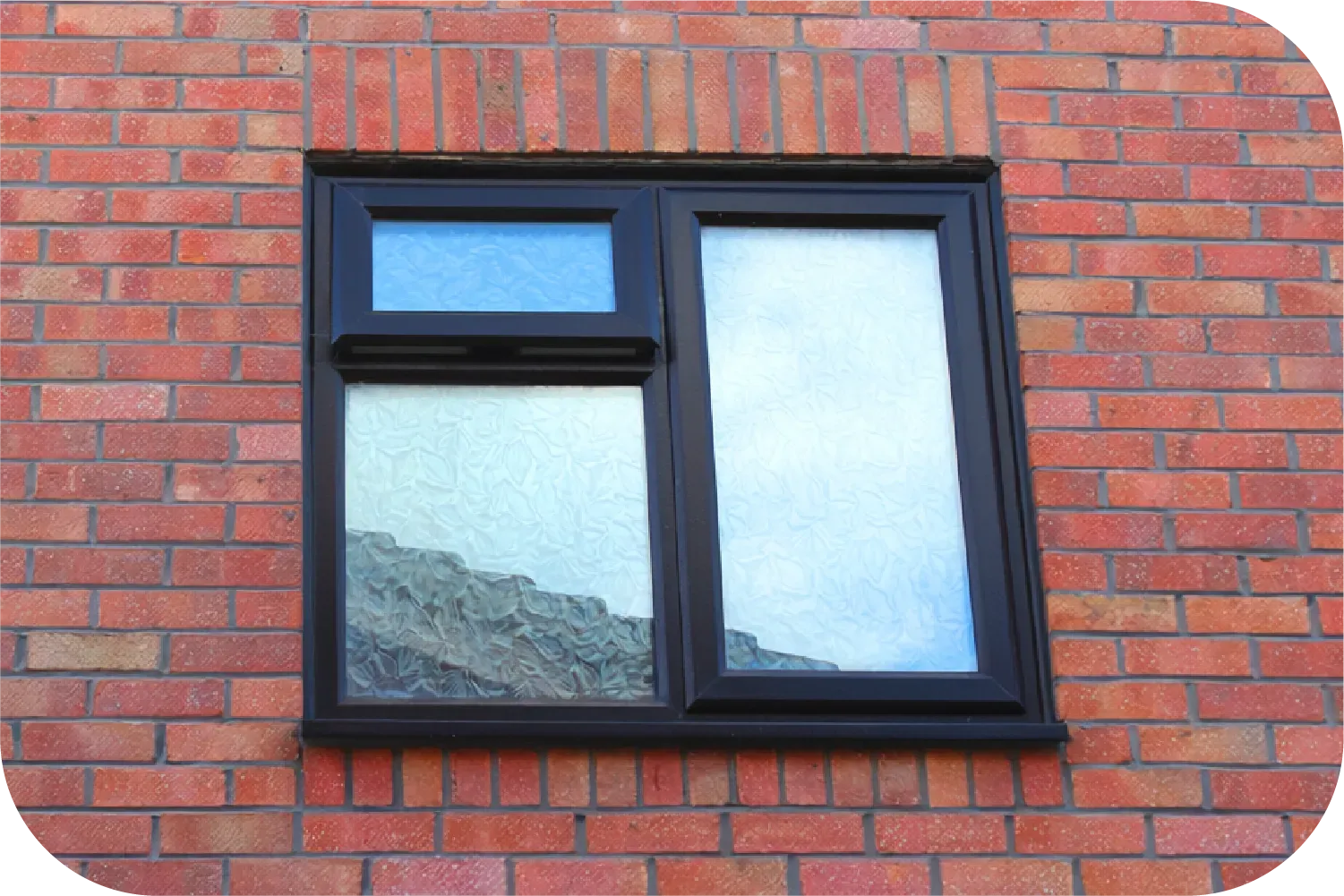A black-framed window with three glass sections set into a red brick wall.