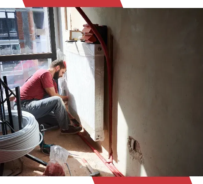 A man is kneeling down next to a radiator in a room.