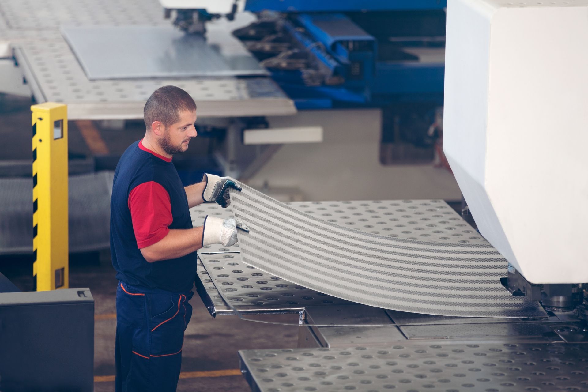 An industrial worker is in action on a metal press machine, holding a piece of steel. An industrial worker is in action on a metal press machine, holding a piece of steel.