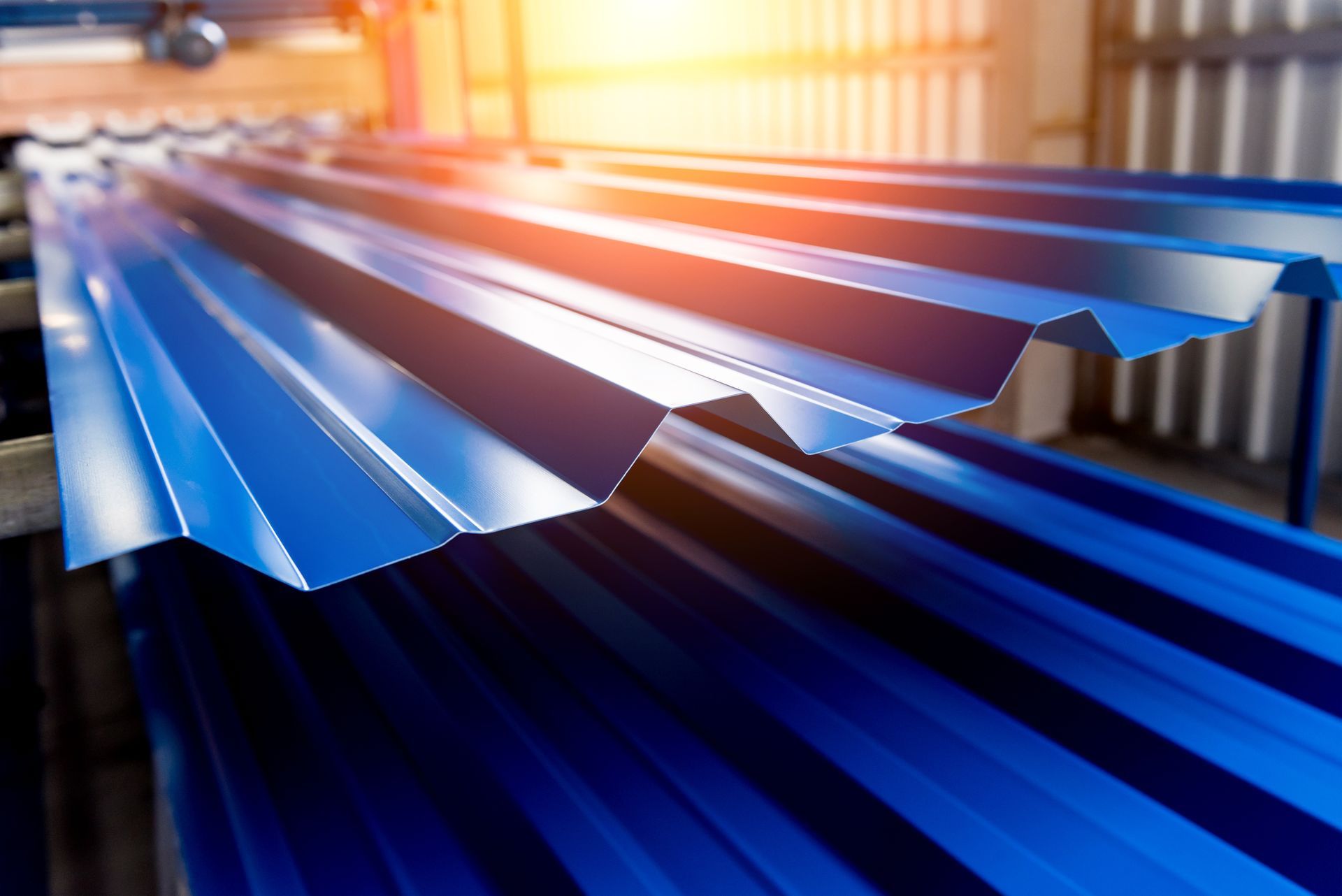 Freshly formed blue corrugated metal sheets stacked on a manufacturing line in bright light.