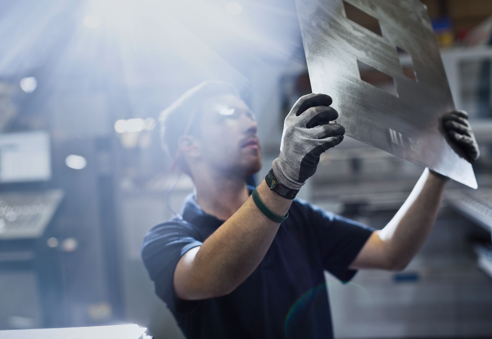 Factory worker examining a large metal sheet under bright industrial lighting. Factory worker examining a large metal sheet under bright industrial lighting.