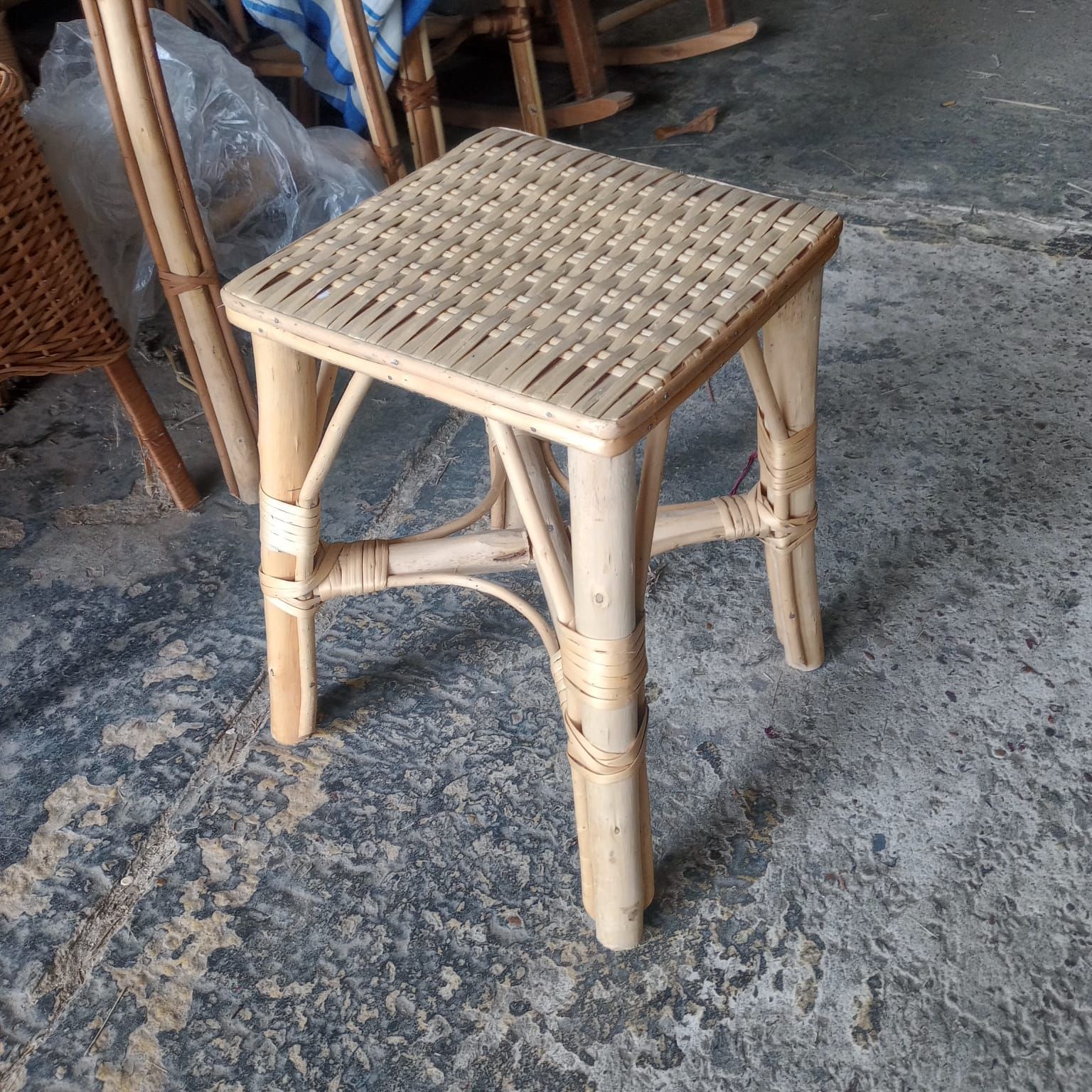 Un taburete de ratán de color claro, con la parte superior cuadrada