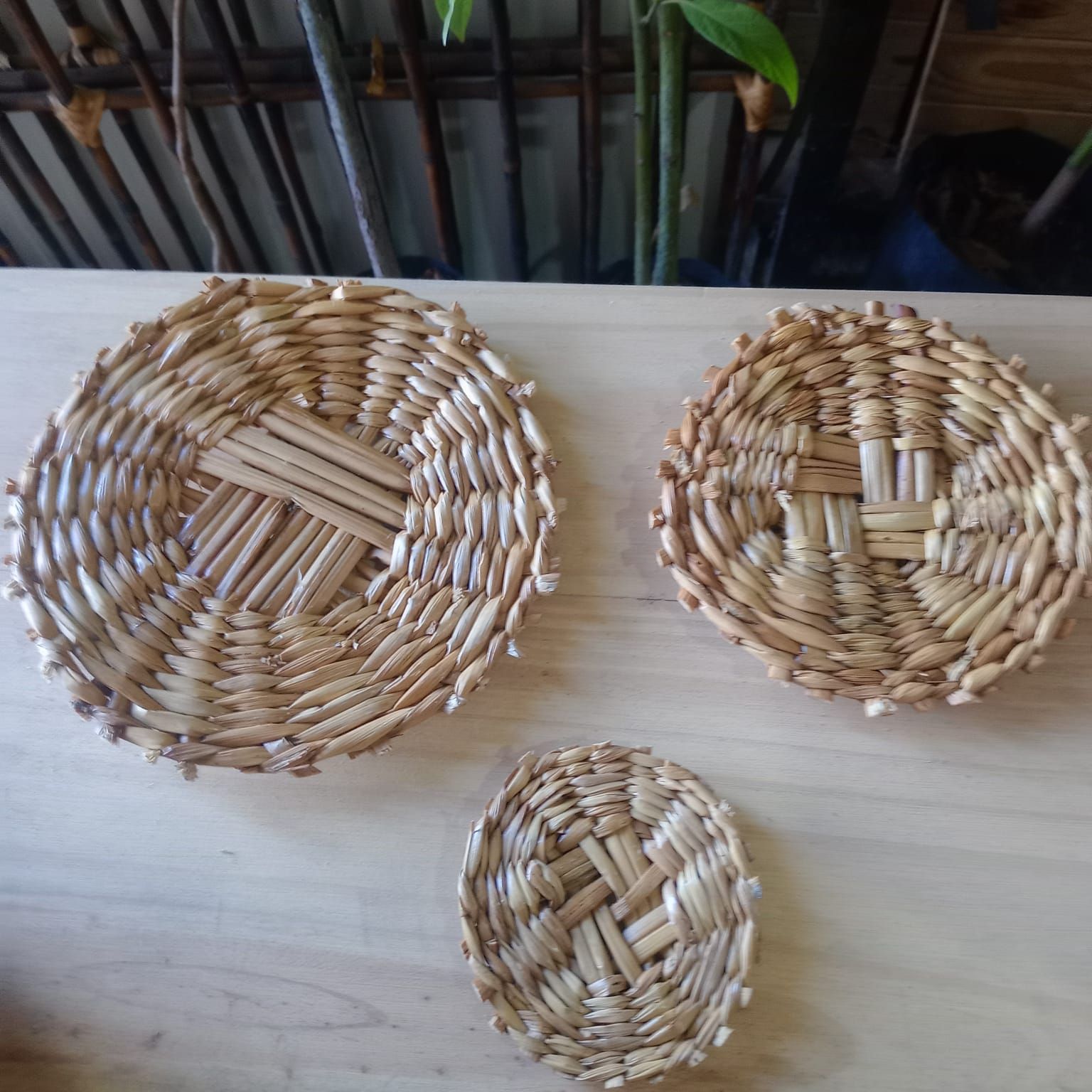 Tres posavasos de mimbre tejido de diferentes tamaños expuestos sobre una superficie de madera clara.