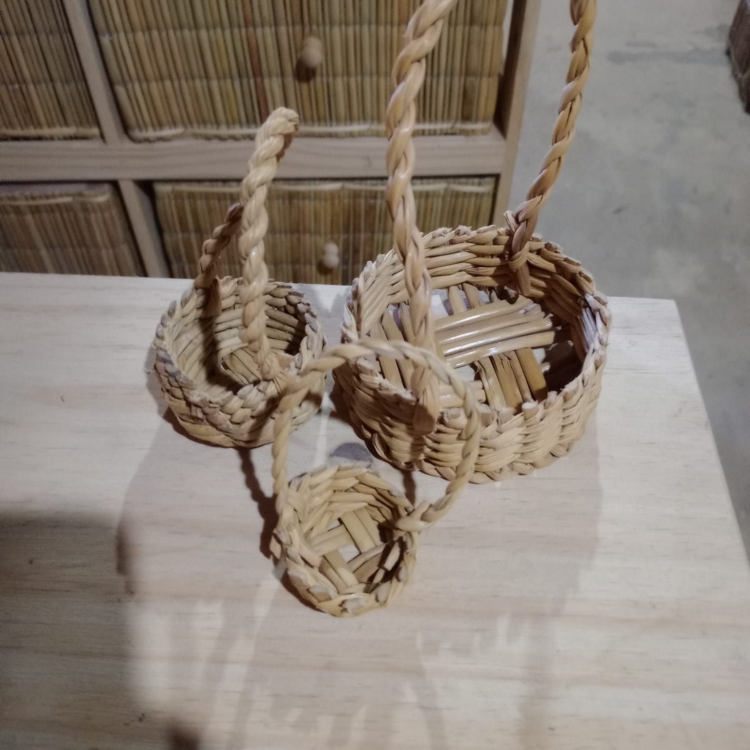 Tres cestas de ratán tejido con asas retorcidas de diferentes tamaños reposan sobre una superficie de madera clara.