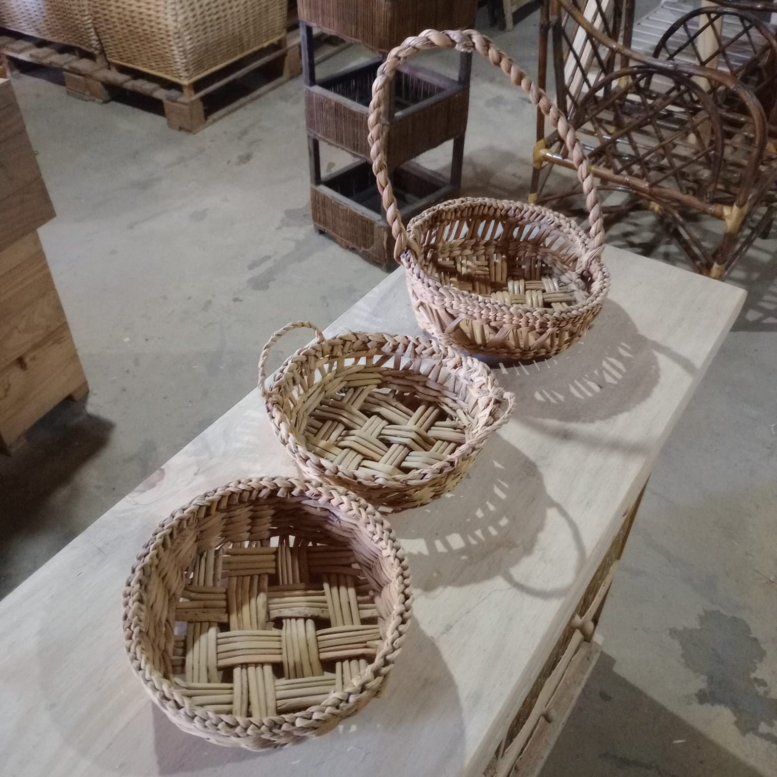 Tres cestas de mimbre tejidas de diferentes tamaños dispuestas sobre una superficie de madera en un taller.