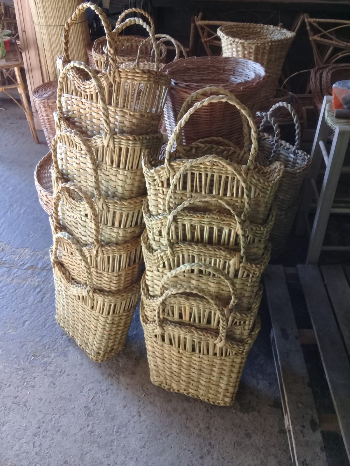 Dos pilas de cestas tejidas de color marrón claro con asas arqueadas reposan en un taller de estilo rústico.