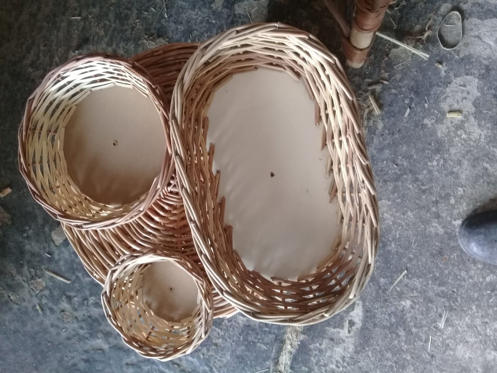 Tres cestas de mimbre tejidas de diferentes tamaños —una ovalada grande y dos redondas más pequeñas— dispuestas en el suelo.