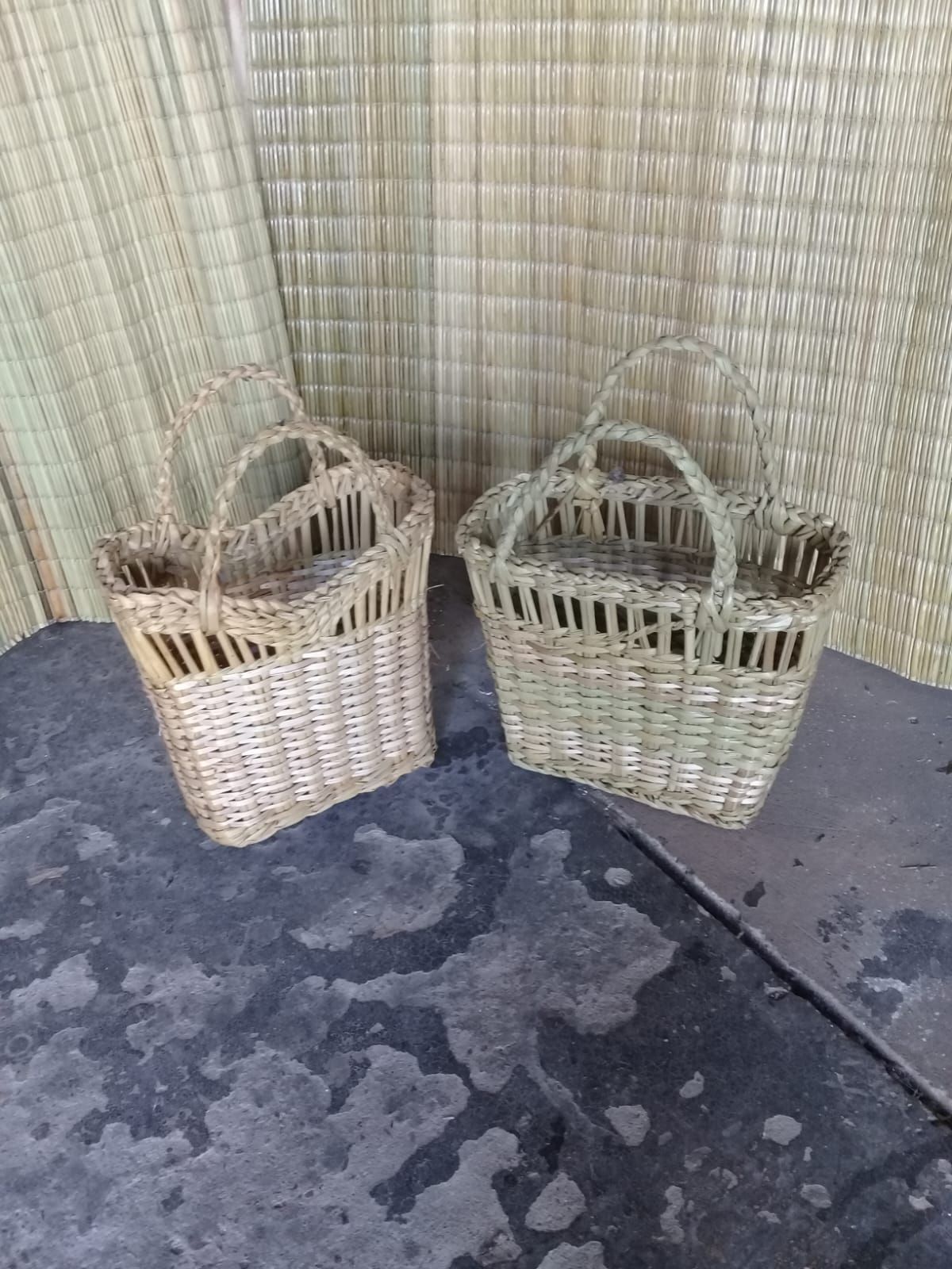 Dos cestas de mimbre tejidas con asas arqueadas se encuentran una al lado de la otra sobre un fondo de esteras tejidas.