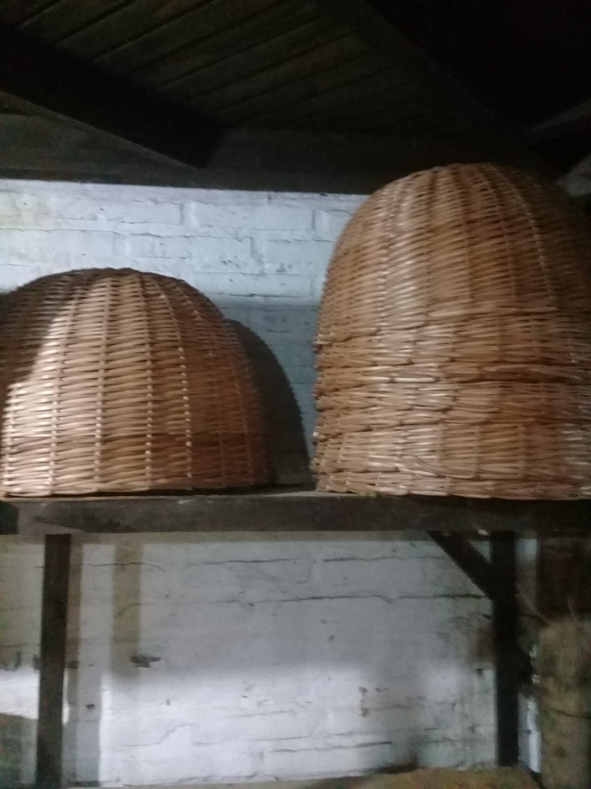 Dos cúpulas de mimbre reposan sobre una repisa de madera junto a una pared de ladrillo blanco en un espacio con poca luz.