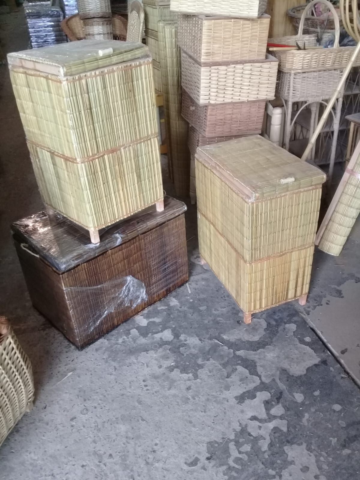 Cestas y baúles de mimbre tejido con tapa apilados sobre un suelo de hormigón en un taller.