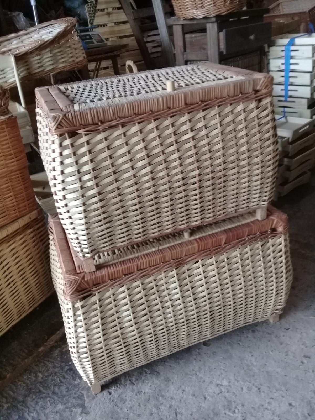 En un taller, dos baúles rectangulares de mimbre tejido con tapa están apilados uno encima del otro.