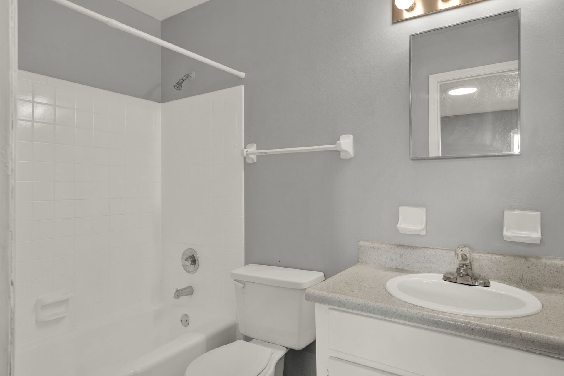 Bathroom with white shower/tub, toilet, sink, and gray walls.