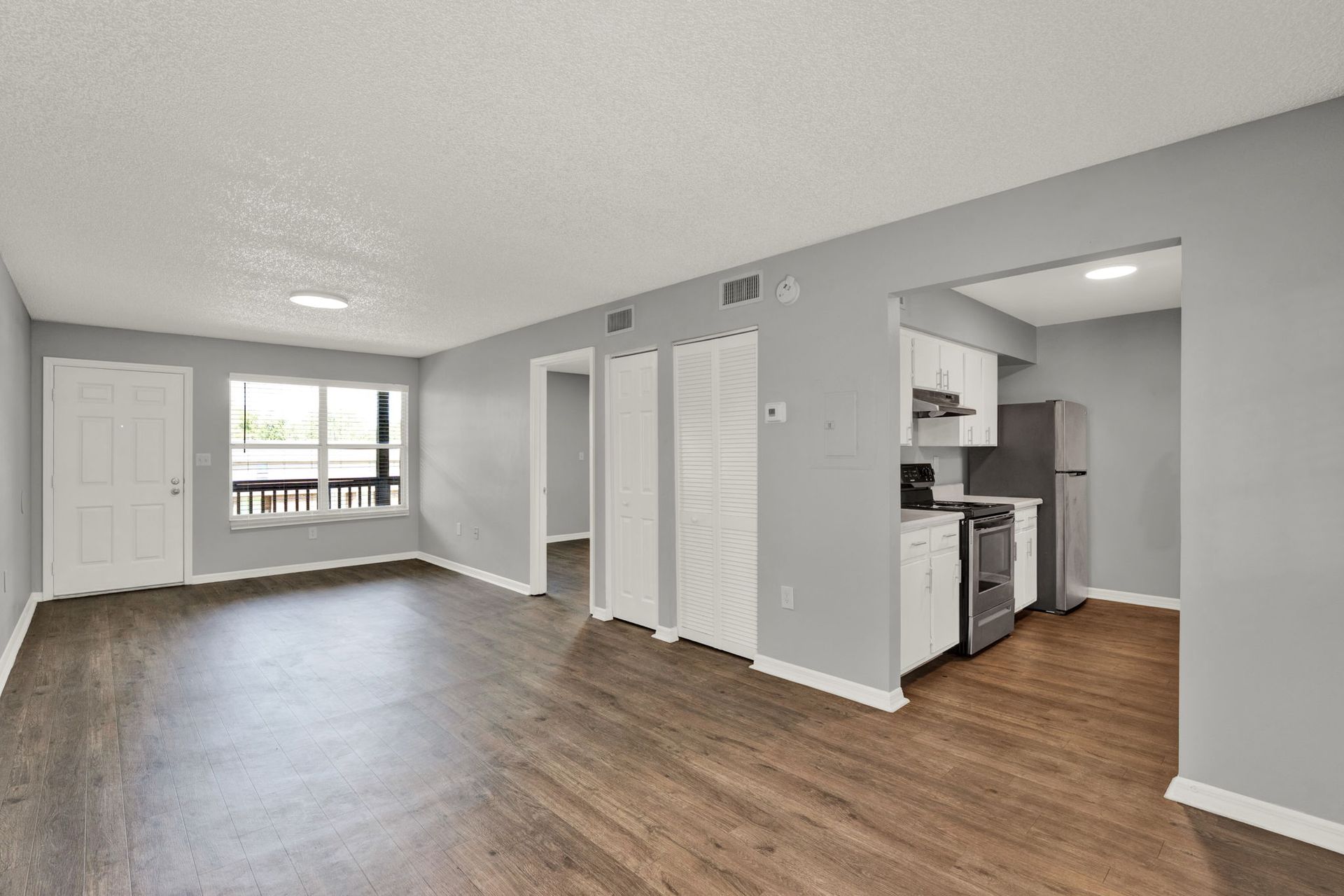 Spacious apartment interior with gray walls, wood-look floors, and a small kitchen area.