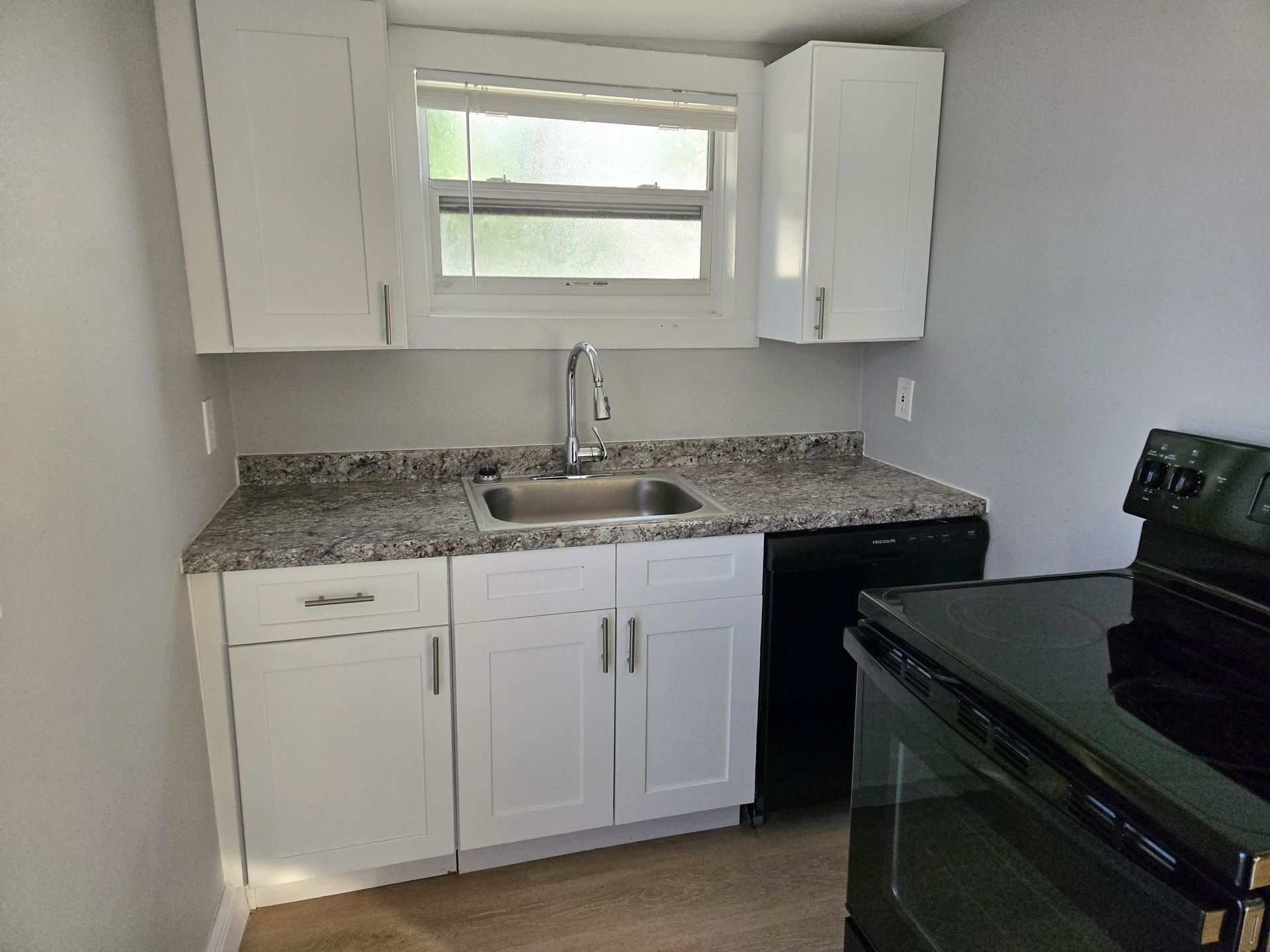 A small, modern kitchen with white cabinets, a granite countertop, and a black stove.