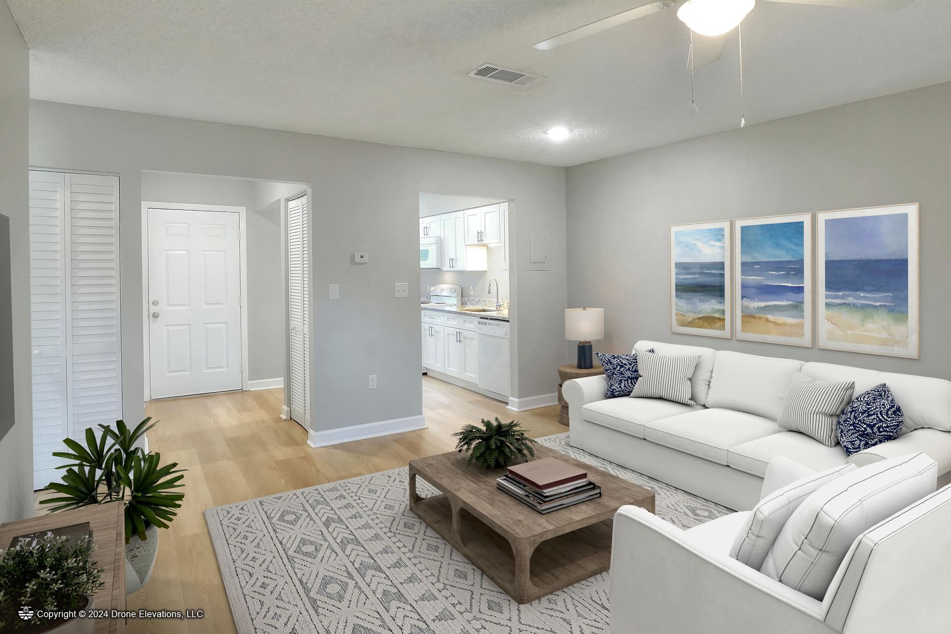 Light-filled living room with white sofa, seascape art, and wood coffee table on rug.