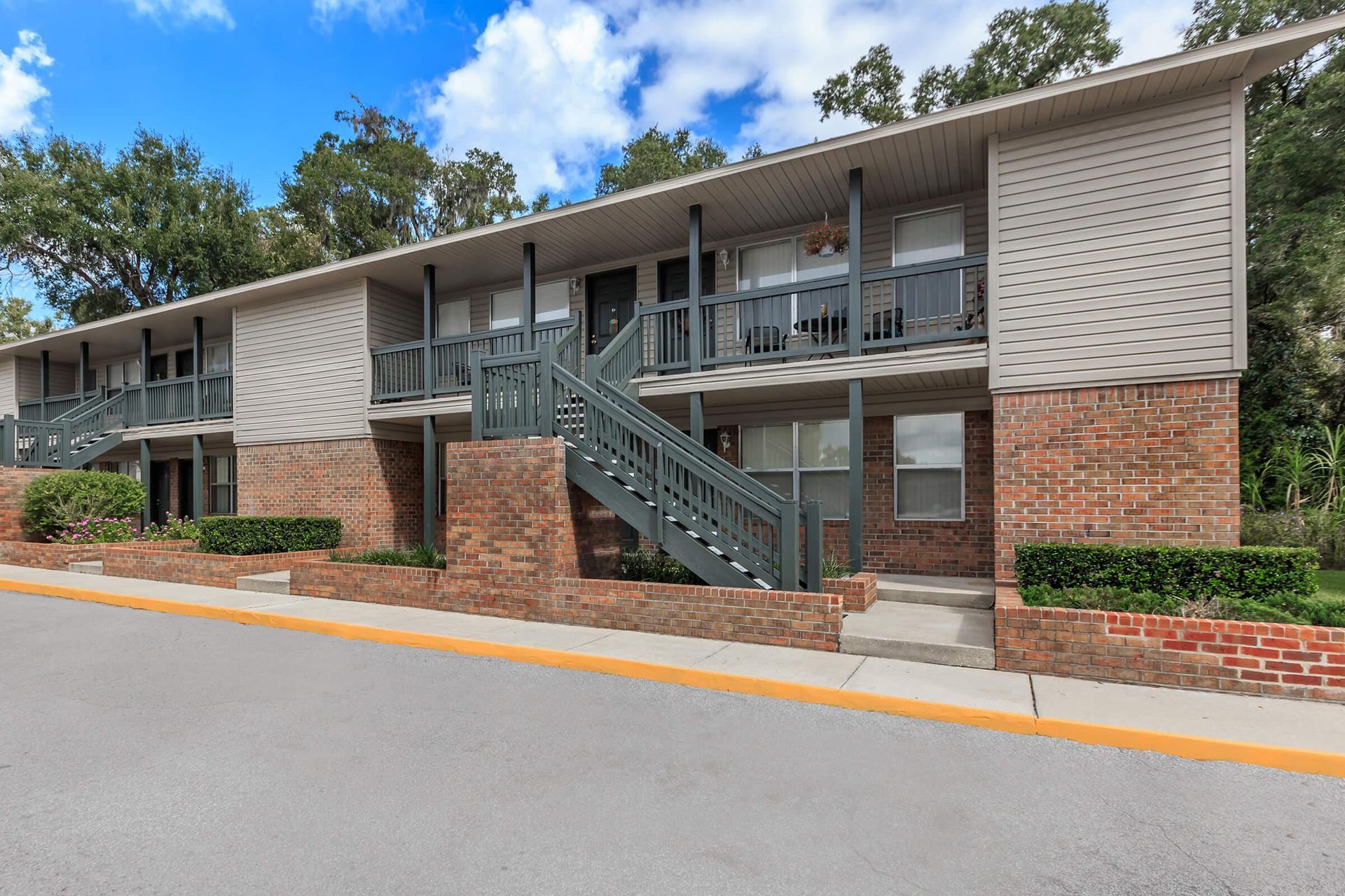 Two-story brick apartment building with gray stairs and balconies, set against a blue sky.
