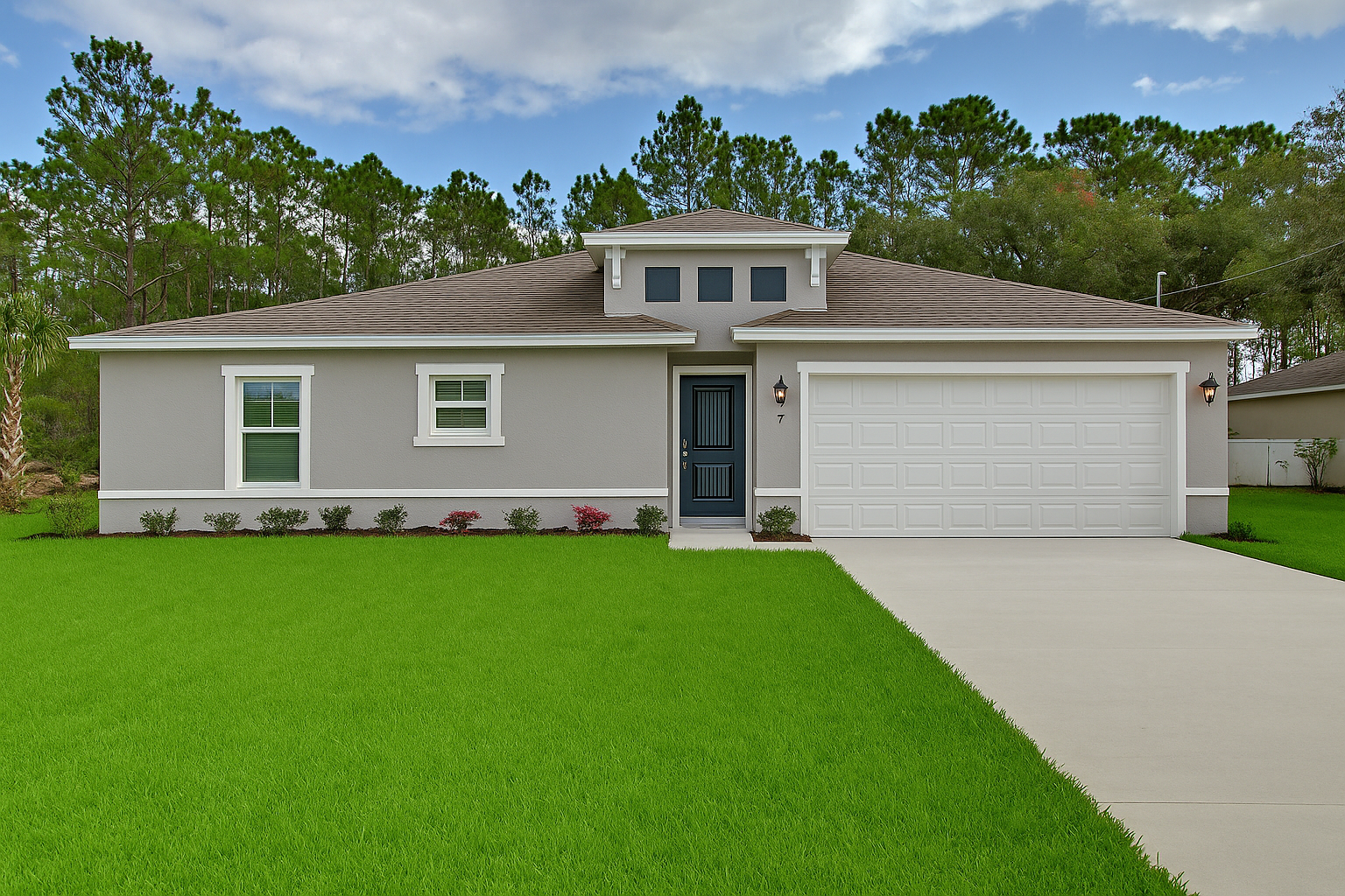 Light gray one-story house with a green lawn and a concrete driveway, trees in the background, and a blue sky.