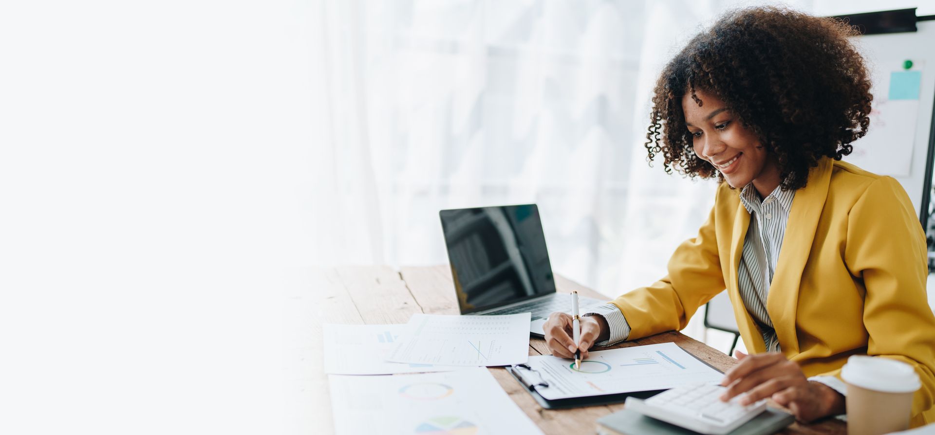 Couple at table with laptop, reviewing documents, smiling. Modern interior with window and plants.