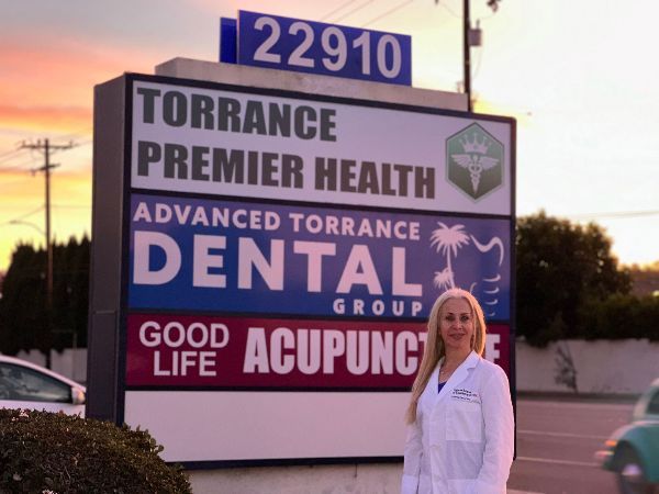 A woman stands in front of a sign for torrance premier health dental group