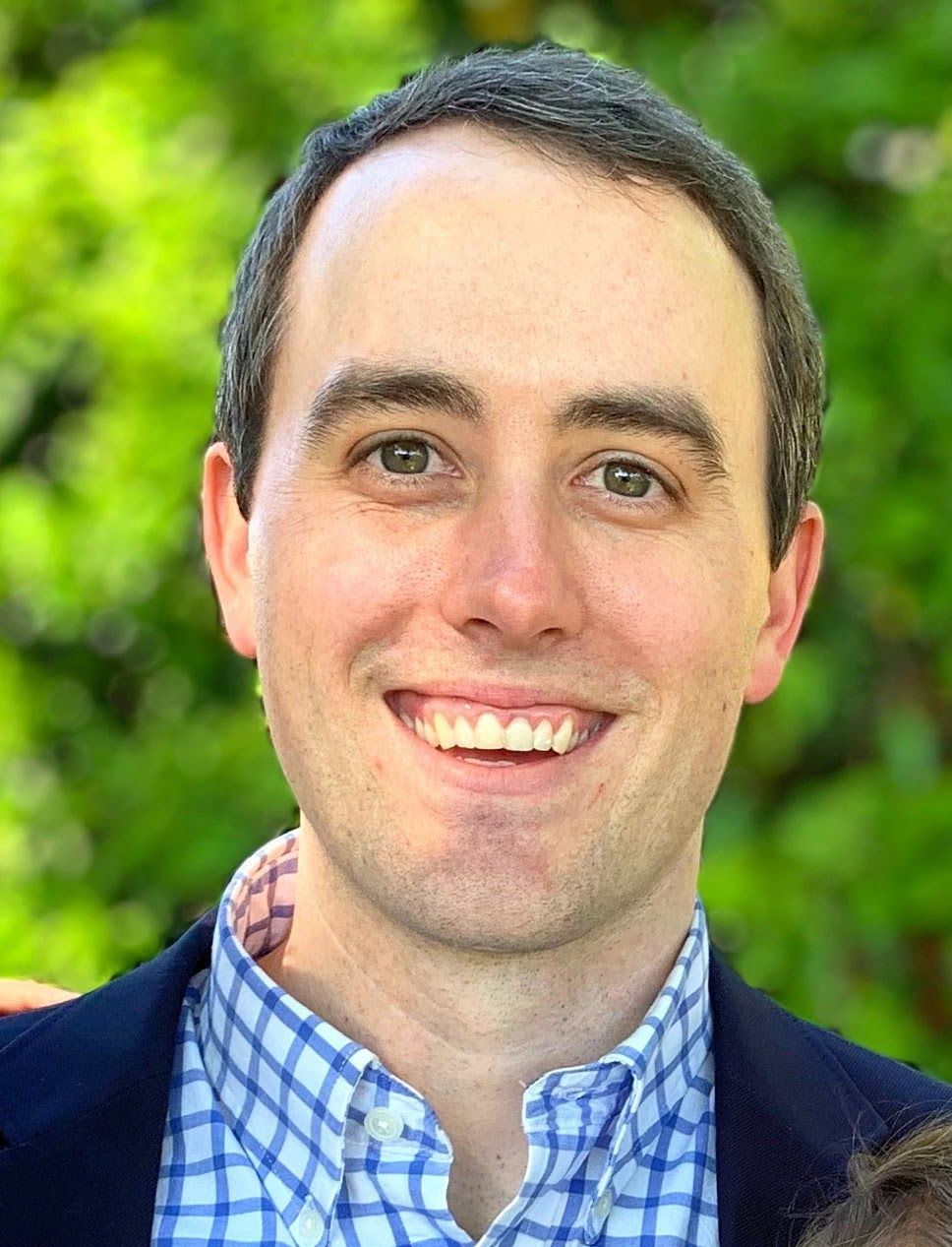 A man in a suit and plaid shirt is smiling for the camera.
