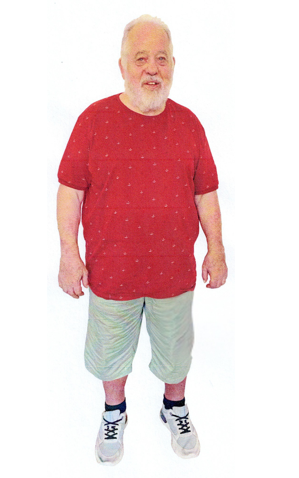 Lächelnde Frau, trägt ein schwarzes Hemd, einen Schal und blaue Jeans, die Hände in den Taschen, steht vor weißem Hintergrund.