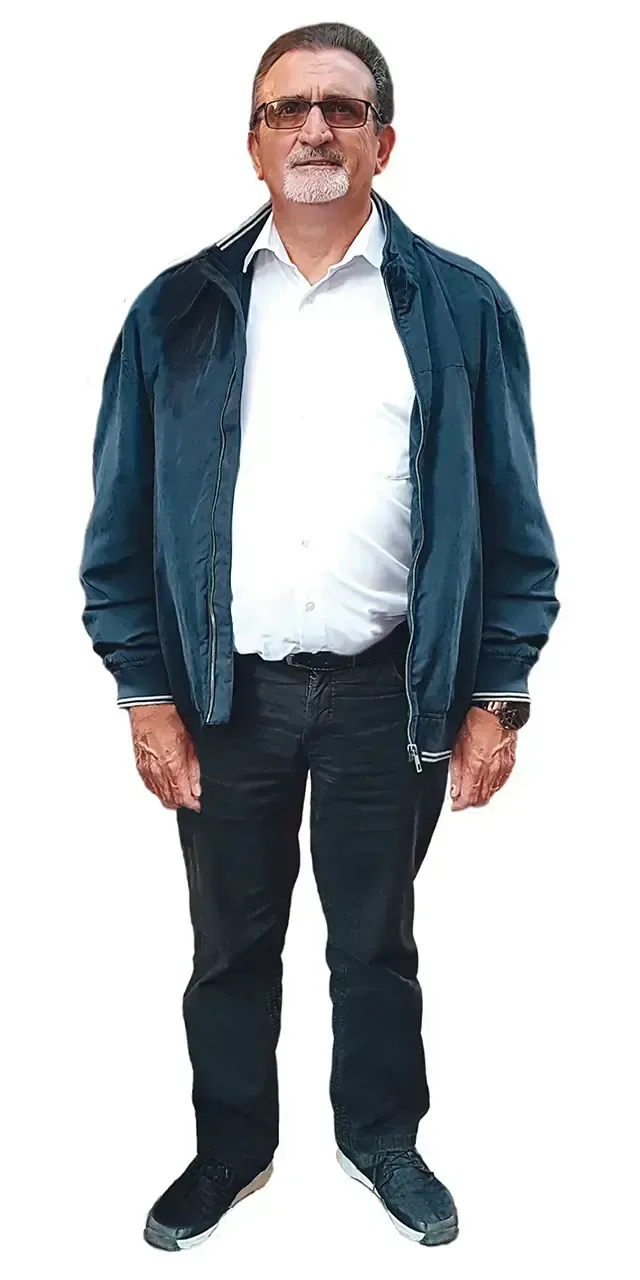 Stehender Mann, trägt eine blaue Jacke über einem weissen Hemd, dunkle Hosen und eine Brille.