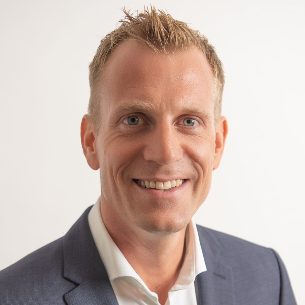 Lächelnder blonder Mann in blauem Blazer und weissem Hemd.