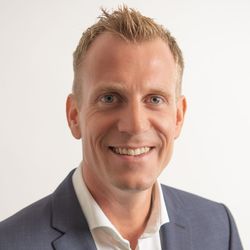 Lächelnder blonder Mann in blauem Blazer und weissem Hemd.