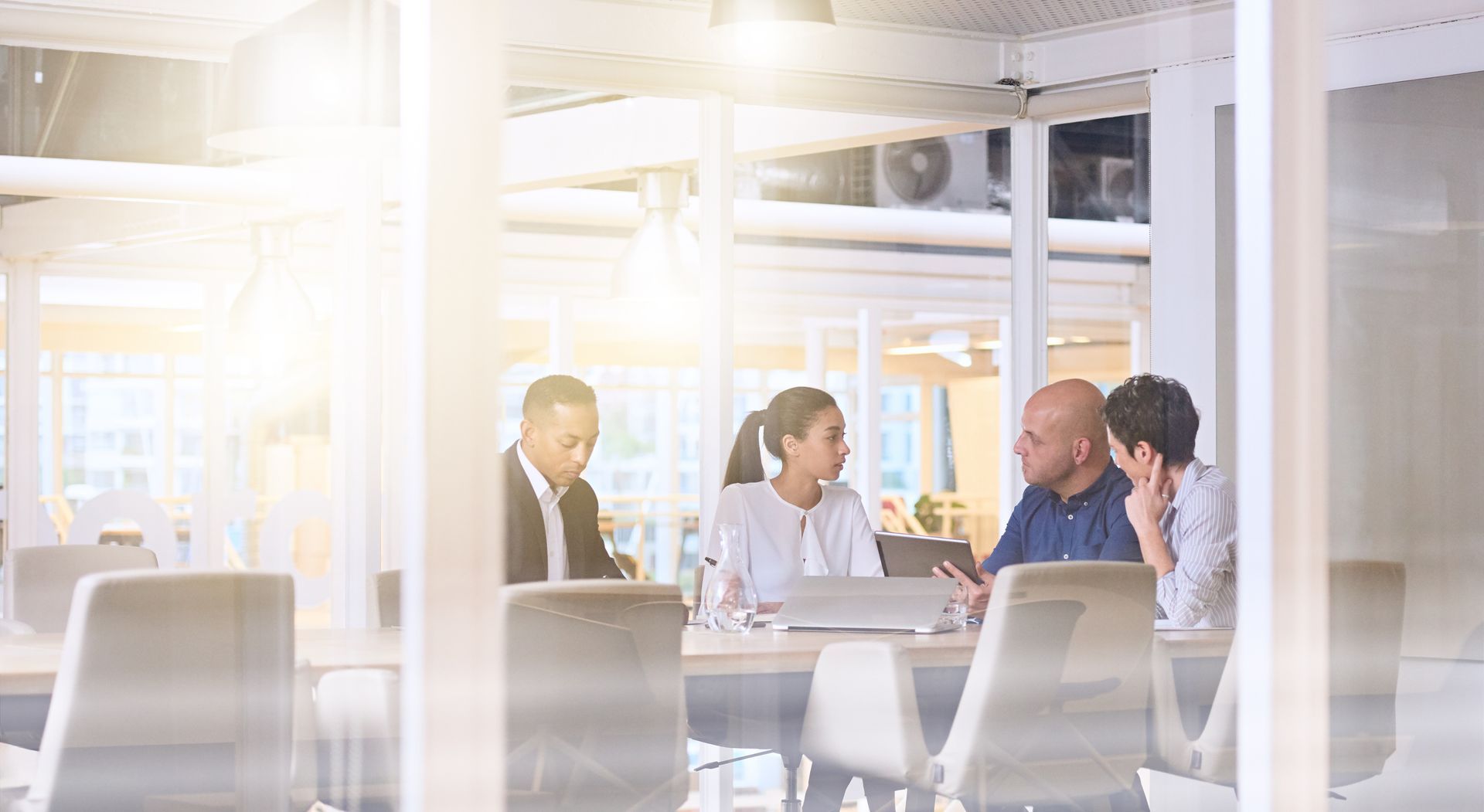 Four people in an office meeting around a table, collaborating with a laptop.
