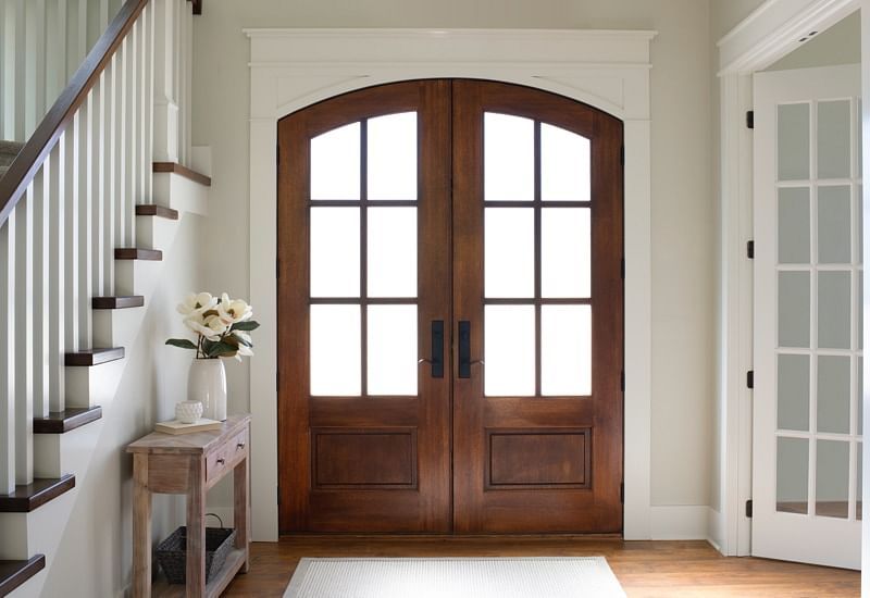 Wooden double doors with arched tops, glass panels, and a white trim. Hallway with staircase and console table.