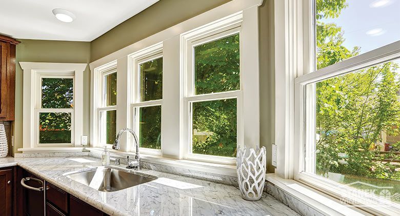Kitchen with multiple white-framed windows overlooking greenery, with a sink and countertop.