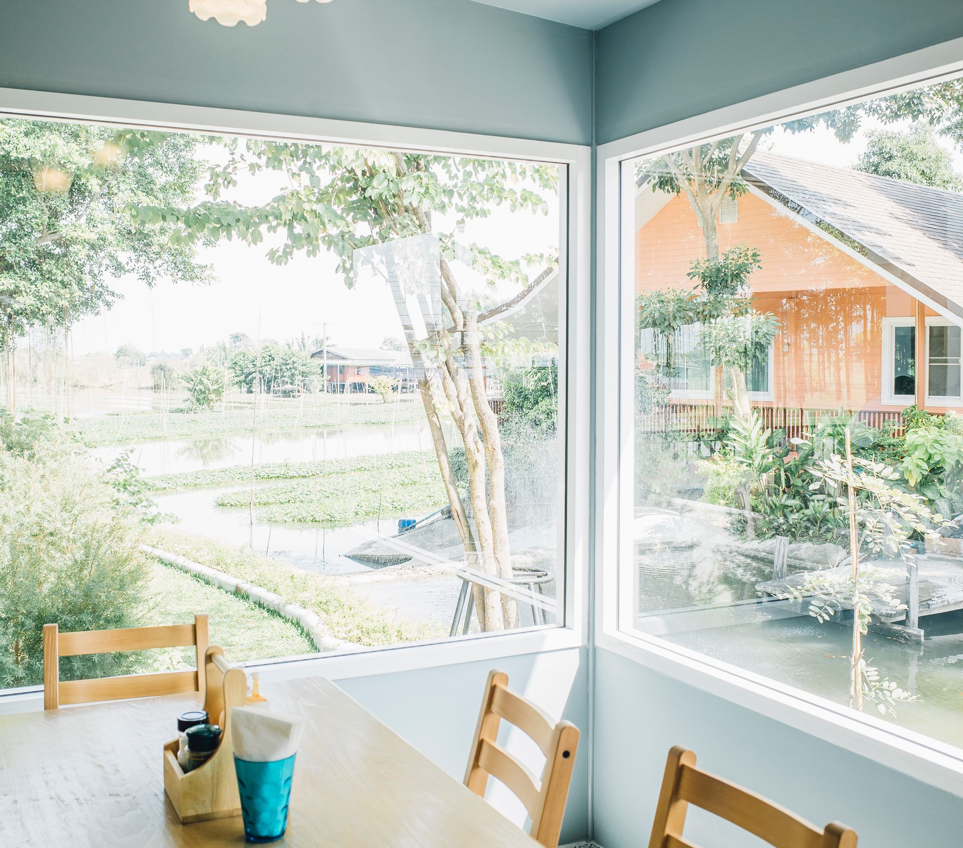 Dining area with large windows overlooking a pond and an orange building. Wooden chairs and table visible.