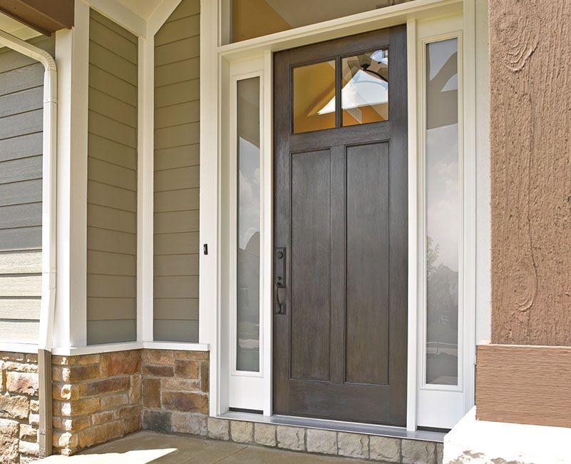 Brown front door with sidelights, under a white trim. Stone and green siding on walls.