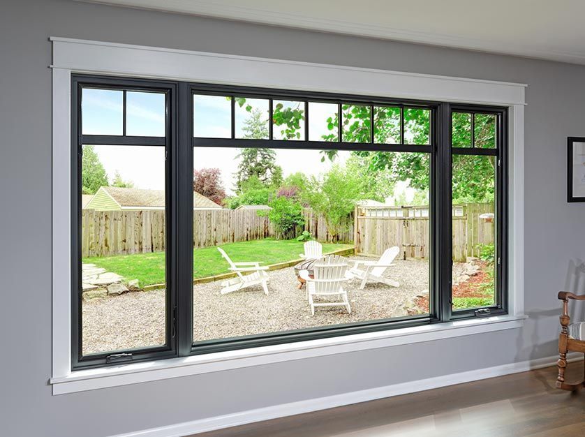 Large black-framed window overlooking a backyard patio with white chairs, green grass, and a wooden fence.