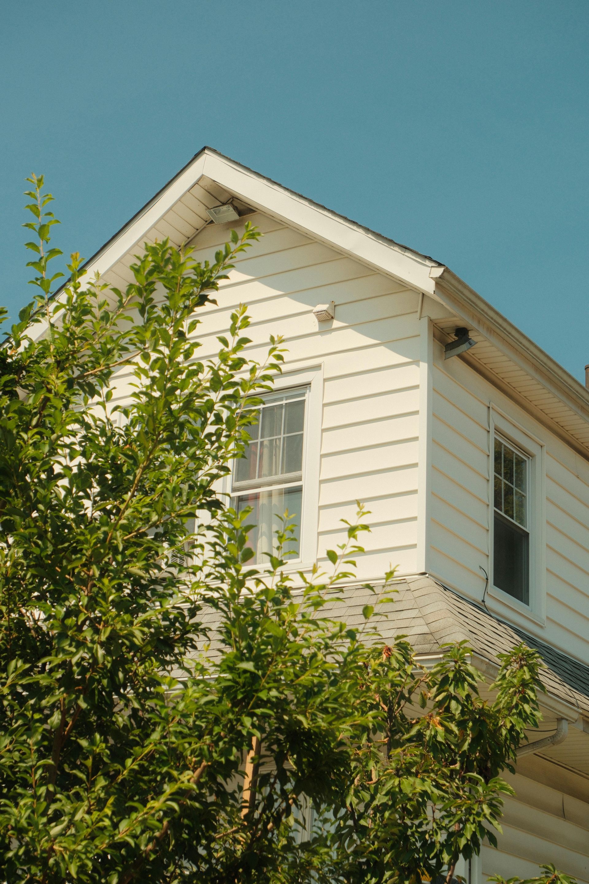Exterior of a white house with a brick column, white-framed windows, and a dark brown roof.