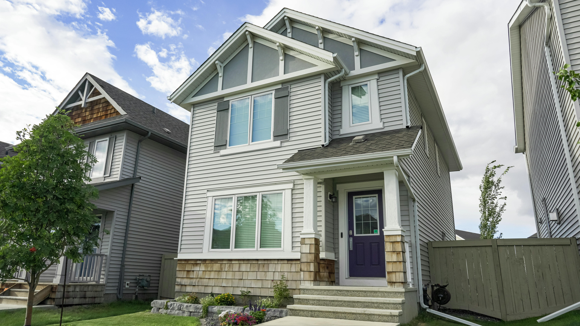Exterior of a white house with a brick column, white-framed windows, and a dark brown roof.