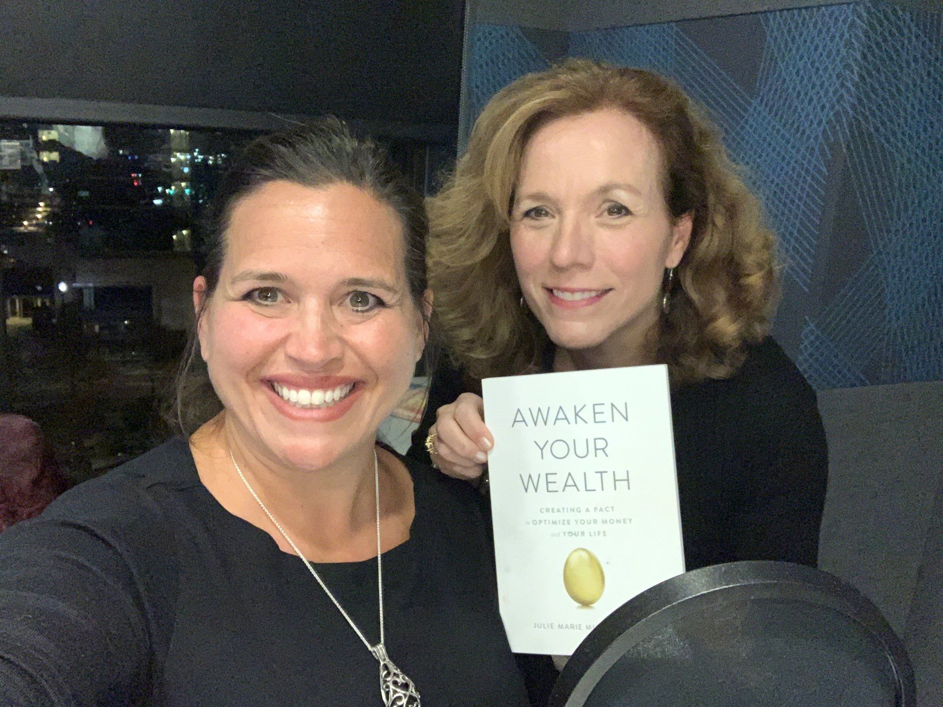 Two women are holding a book titled awaken your wealth