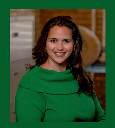 A woman is wearing a green sweater and smiling for the camera.