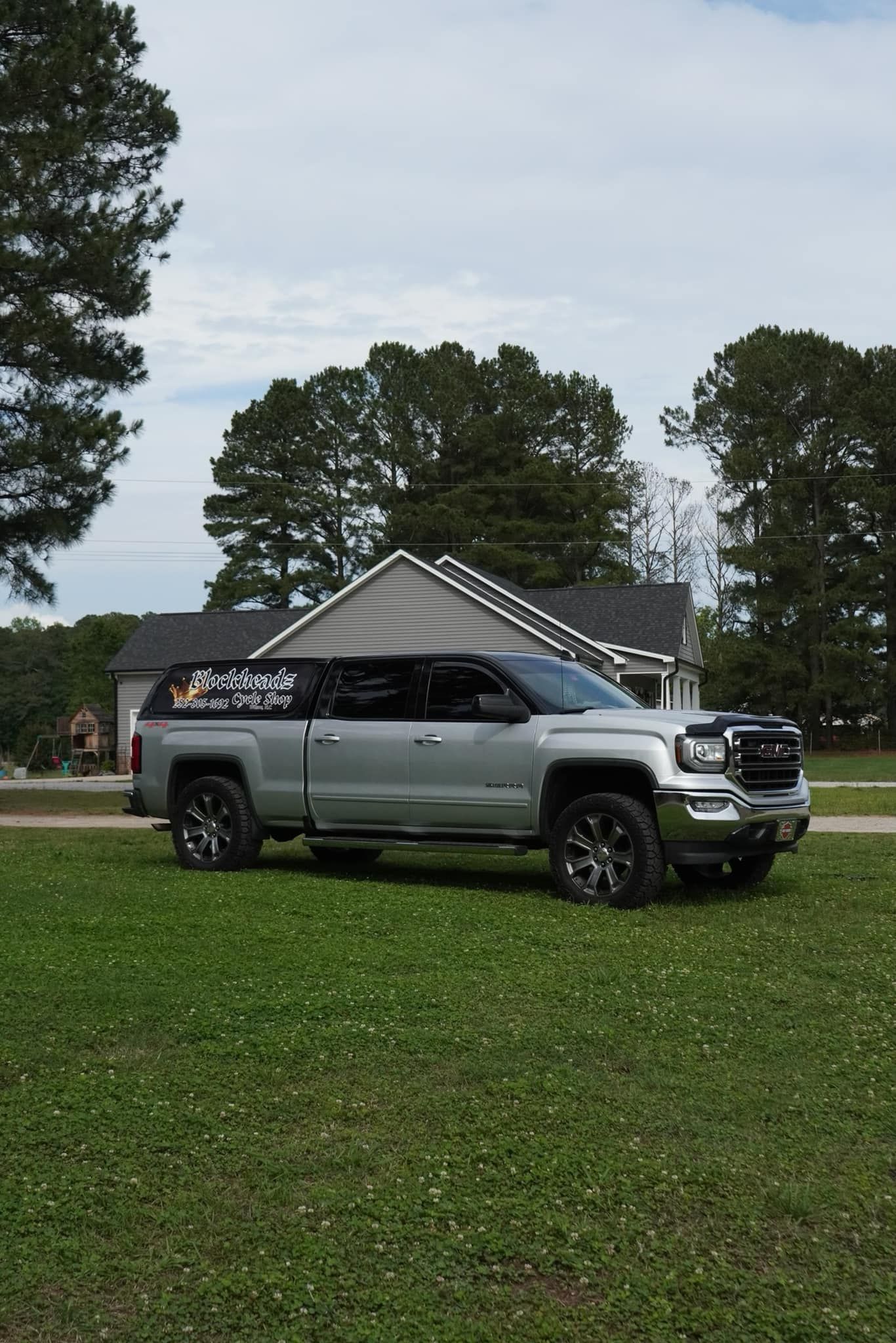 Silver pickup truck parked on green grass; house and trees in background.