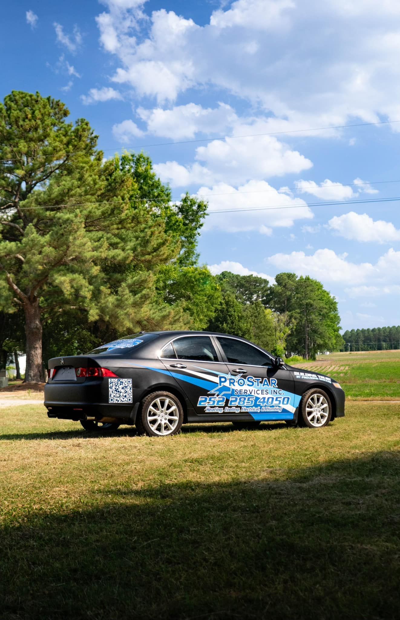 Black car with blue and white graphics on a grassy field with trees and a cloudy sky.