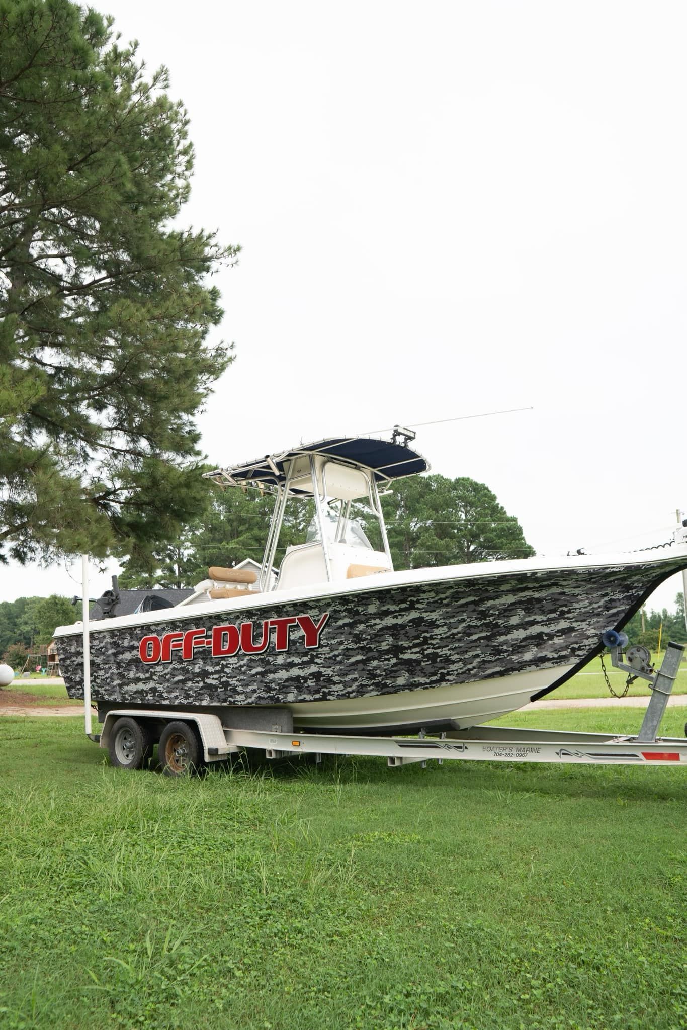 Boat on trailer, covered in black and white camouflage wrap, parked on grass.