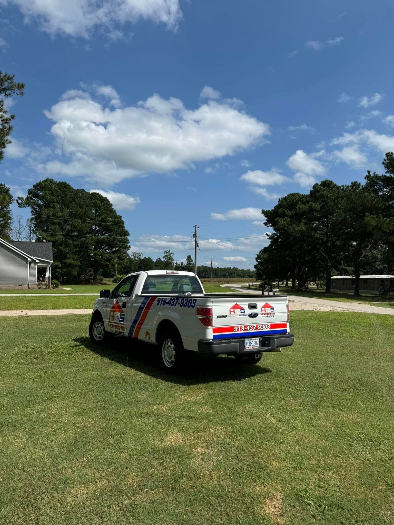 White pickup truck parked on green grass under a blue sky with fluffy clouds.