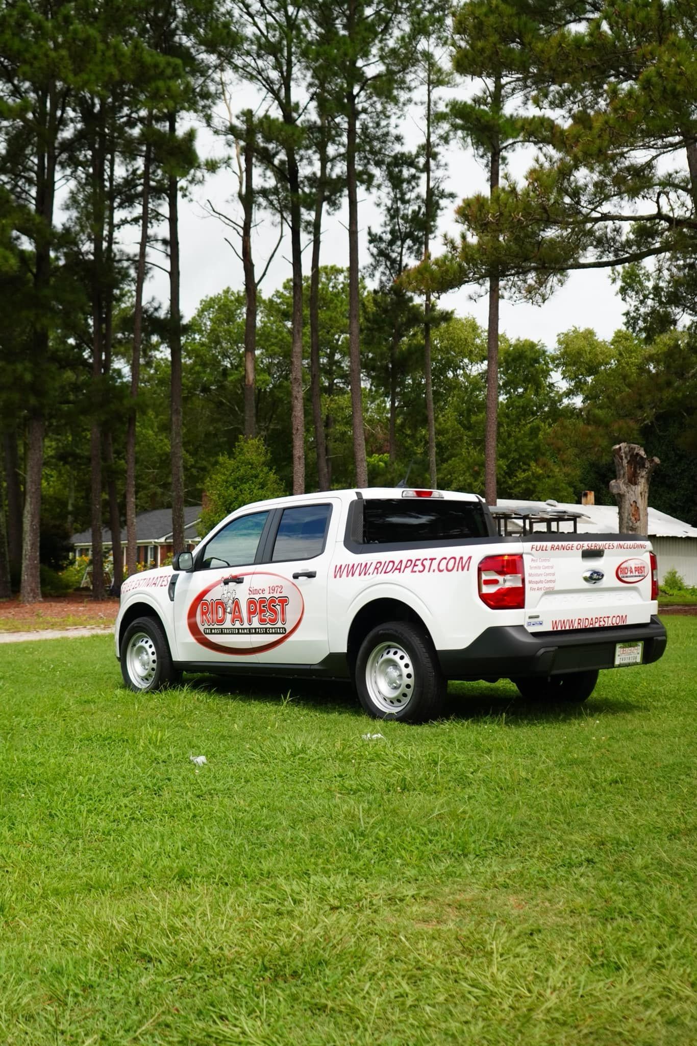White truck with company logo parked on grass, trees in background.